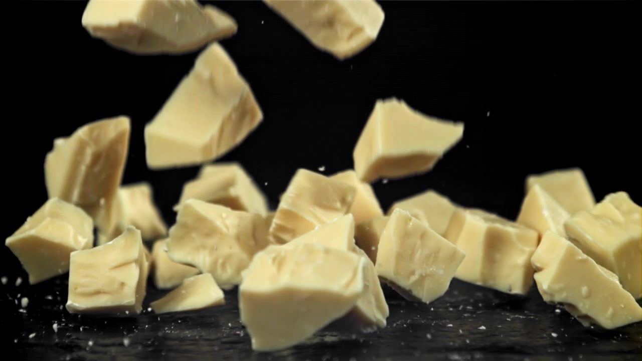 Chute de morceaux de chocolat blanc au ralenti sur fond noir