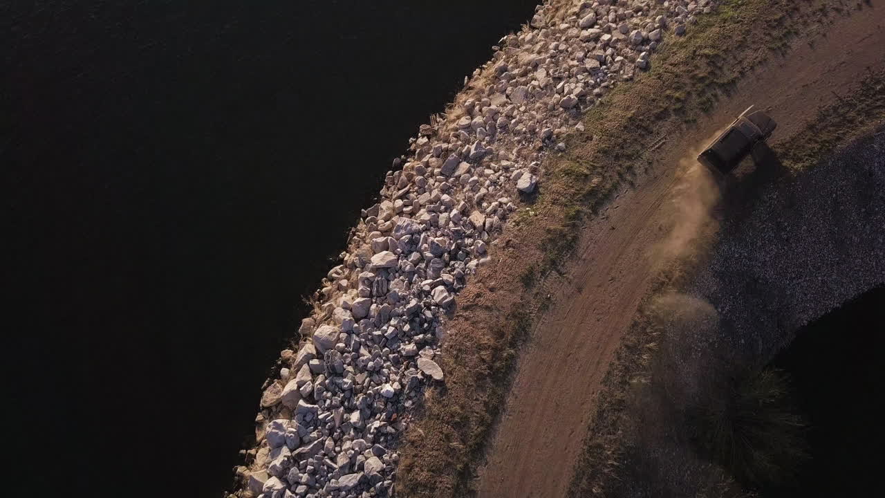Quick drone flyover view of an old pickup truck driving around a curve on a jetty sea wall breakwater at sunset
