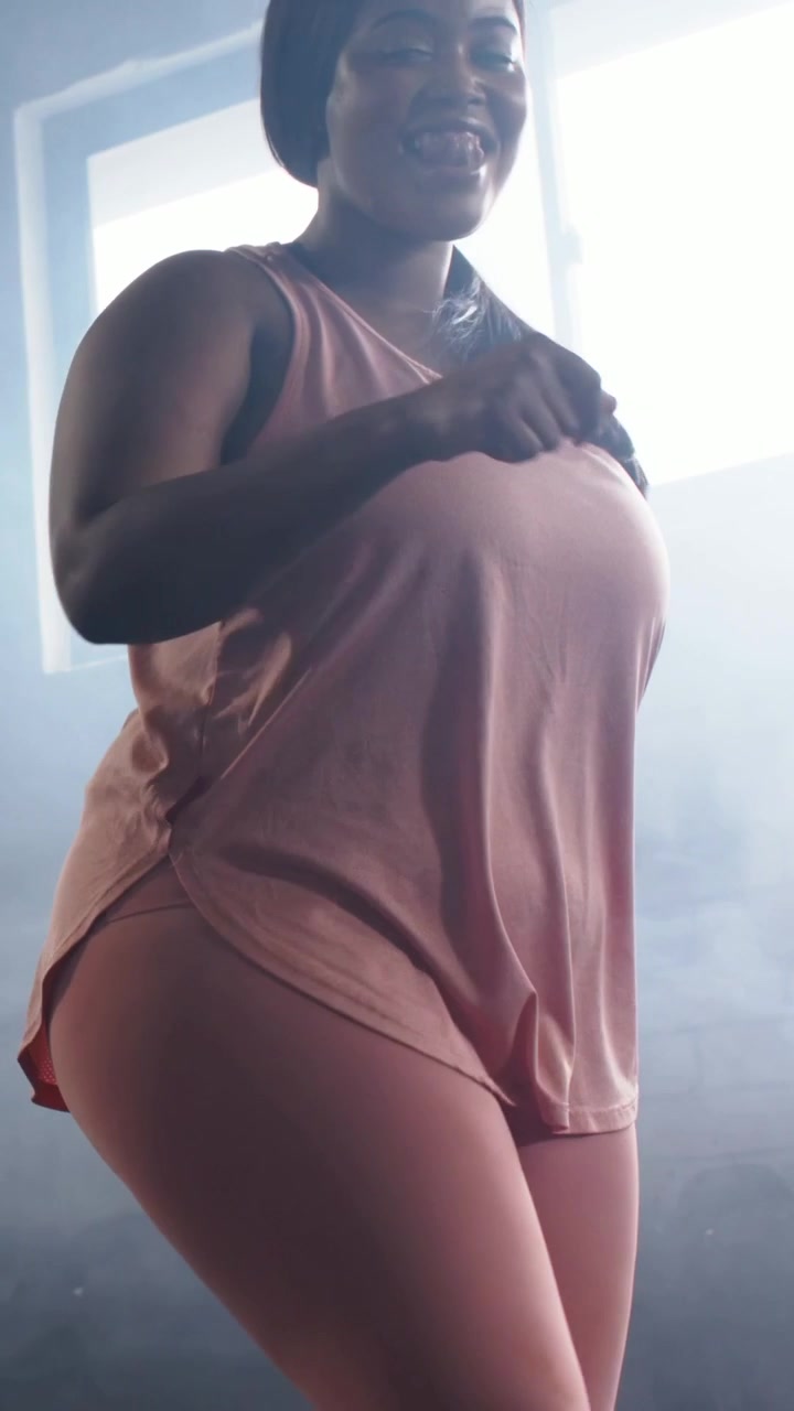 Video verticale: Donna di mezza età con canotta rosa che controlla l'orologio, iniziando una breve routine in uno studio sfocato.