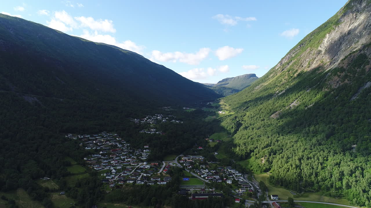 un avión no tripulado se acerca a una pequeña ciudad noruega en un valle verde rodeado de escarpadas montañas.