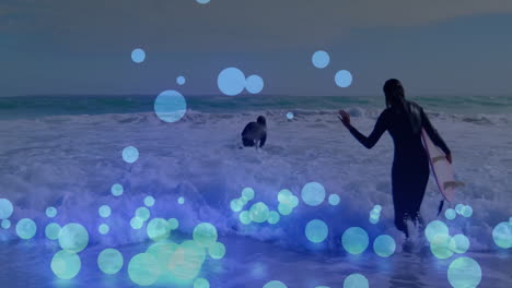 two surfers paddling and wading into foamy ocean waves, showcasing tech using blue circle overlays