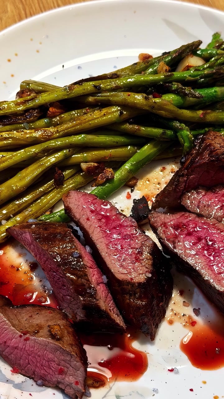 Steak slices and sautéed asparagus served on a white dinner plate at a table