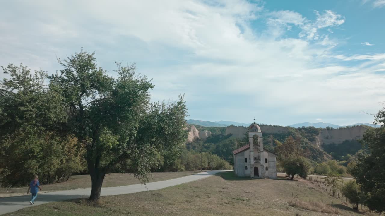 Casual woman walks to church on scenic country lane with landscape views PAN SHOT