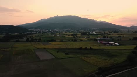 Retracción-Aérea-De-La-Montaña-Y-El-Pueblo-En-El-Campo-Al-Atardecer,-Pangaio,-Grecia