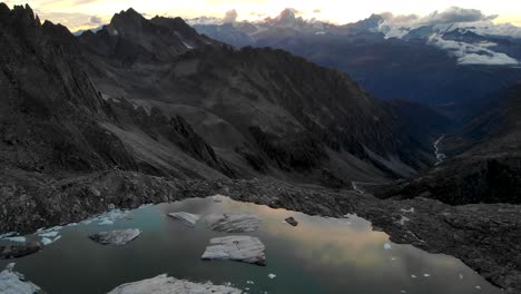 Aerial-flyover-above-a-lake-full-icebergs-from-a-melting-glacier-in-remote-parts-of-the-Swiss-Alps-with-a-sunset-reflection