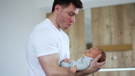 caring caucasian man swaying his newborn son in hands. little child wakes up and dad smiles to him. blurred backdrop.
