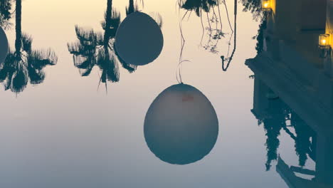 Swimming-pool-water-reflection-of-a-party-in-a-tropical-place-with-balloons-and-palm-trees,-4K-shot