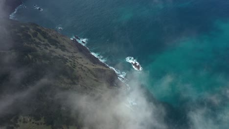 drone shot of the cliff side of espigao amorelo in madeira moving down through the thin clouds and tilting downwards to reveal the cliffside and colorful ocean.