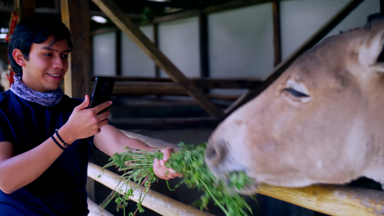 молодой улыбающийся мужчина кормит обезьянку на ферме и фотографирует на телефон
