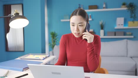 asian woman ringing phone and having angry conversation while working from laptop