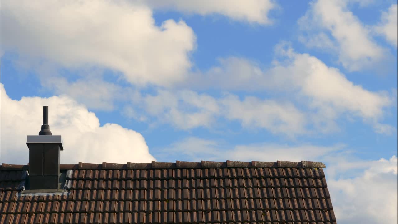 Time lapse shot of flying white clouds on blue sky behind rooftop of house