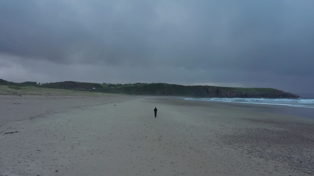 hombre solitario caminando en la playa de arena de playa de xago con nublado en asturias, españa