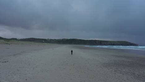 lone man walking on sandy beach of playa de xago with overcast in asturias, spain