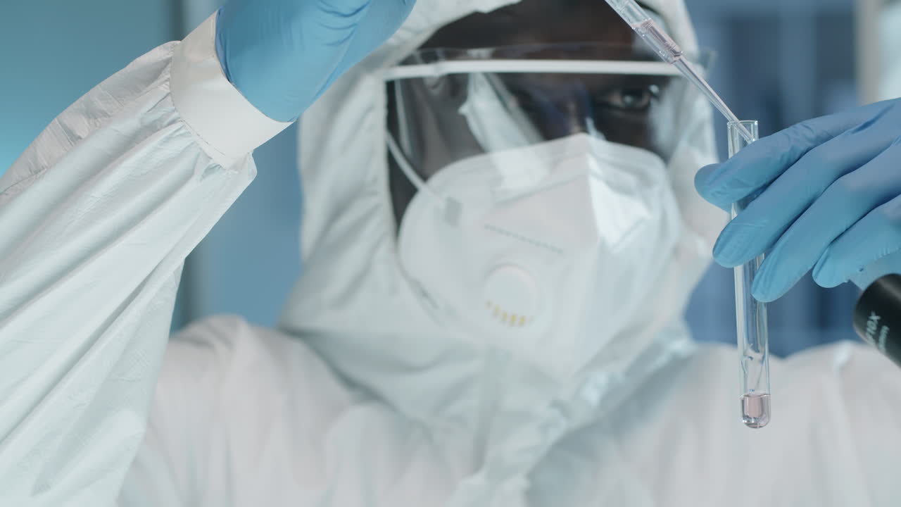 Scienziato di colore in laboratorio in tuta protettiva che esegue un esperimento chimico