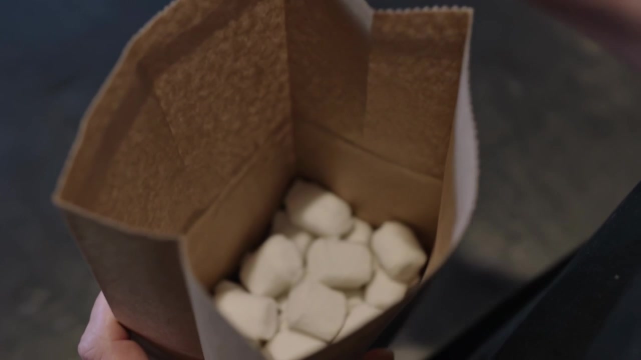 Packing aproned masked barista placing marshmallows into brown bag at cafe counter for order