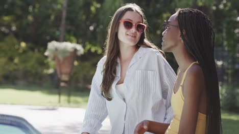 happy diverse teenage female friends in sunglasses talking in garden at pool in slow motion