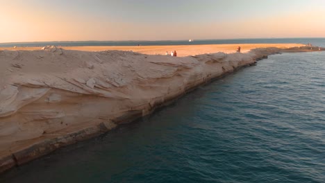 Hombres-De-Oriente-Medio-Vestidos-Con-Kanduras-Caminan-Sobre-La-Increíble-Costa-Erosionada-De-Abu-Dhabi-En-El-Golfo-Pérsico-Durante-La-Puesta-De-Sol