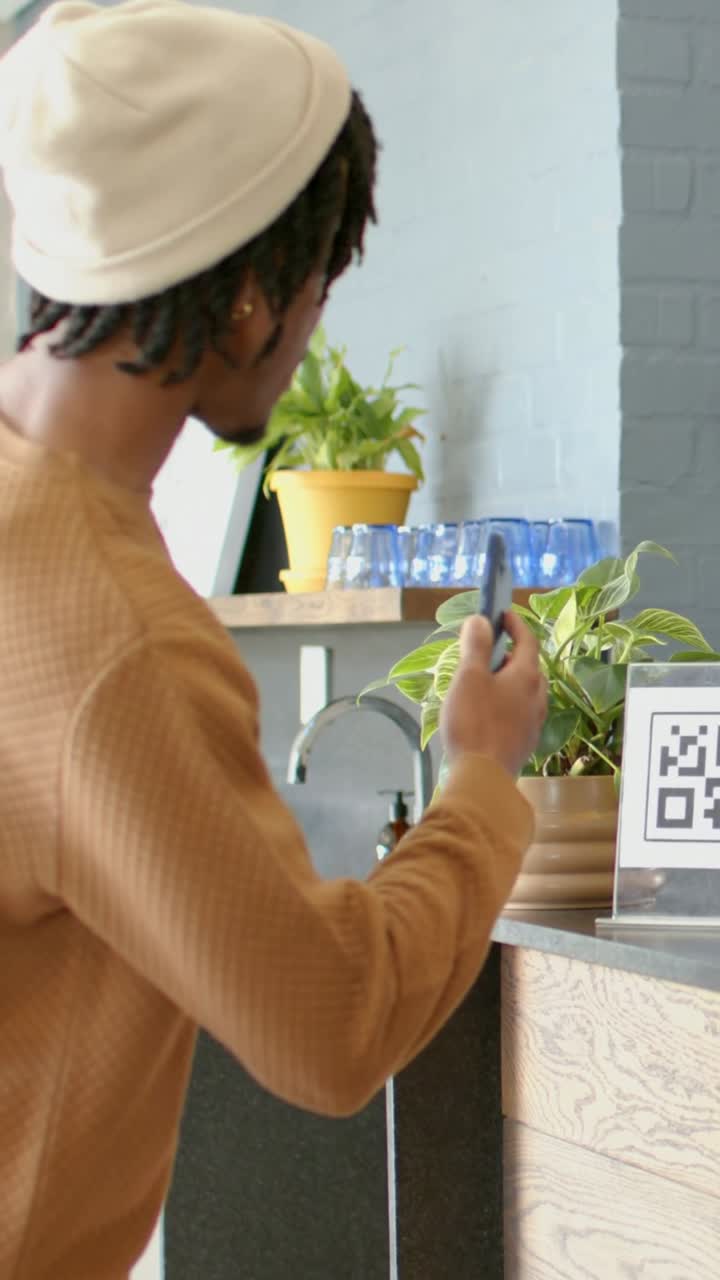 Vertical video: Walking left, man in beanie sweater scanning QR sign with phone at cafe verifying