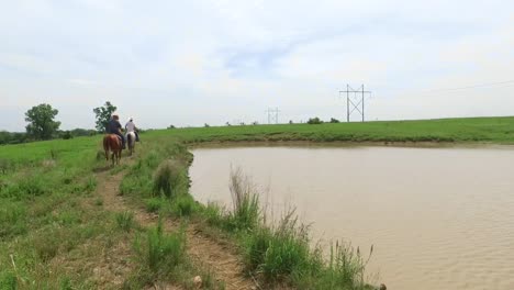 two cowboys on horseback ride away from a waterhole, kansas