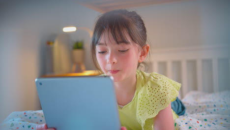 Girl-In-Bedroom-At-Home-Lying-On-Bed-Using-Digital-Tablet