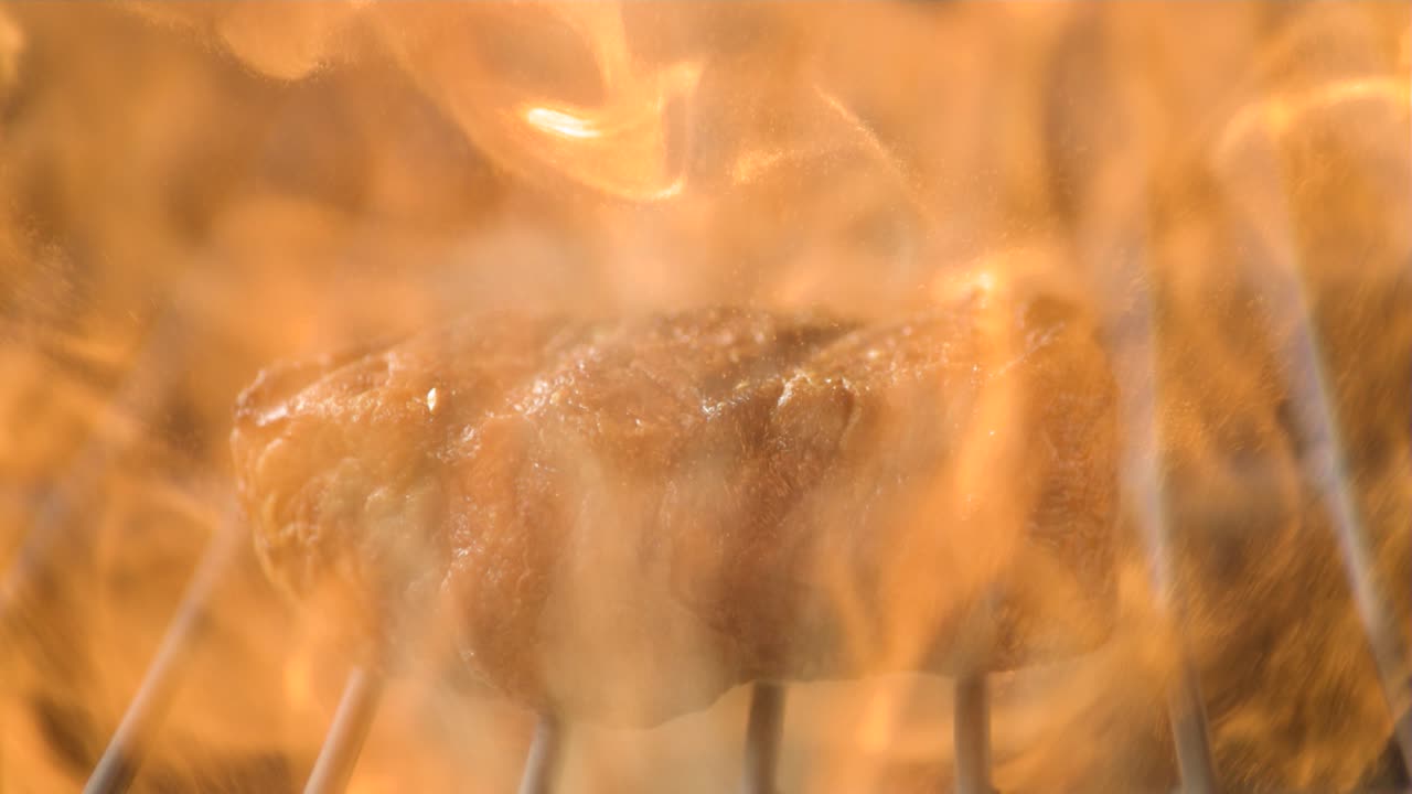 그릴에서 걱거리는 스테이크 클로즈업, 슈퍼 슬로 모션으로 주스와 불꽃을 포착합니다.