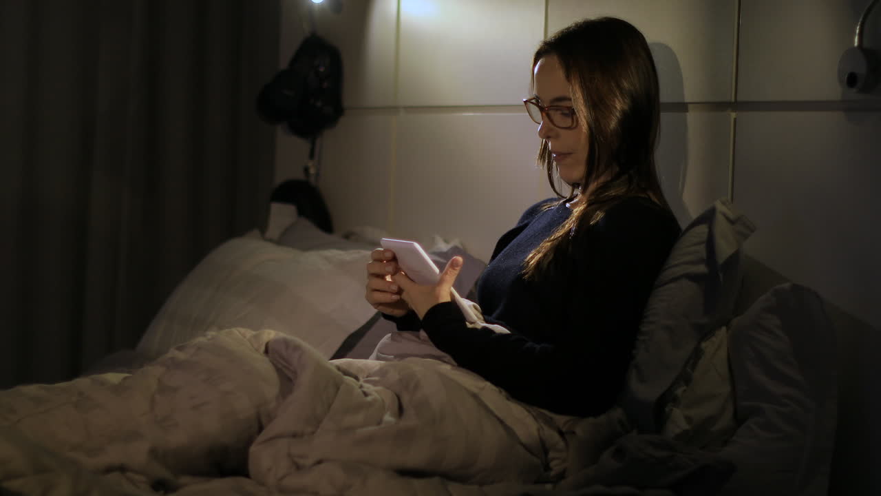 Cozy middle aged adult woman puts on glasses and reads an e-book. Medium shot.