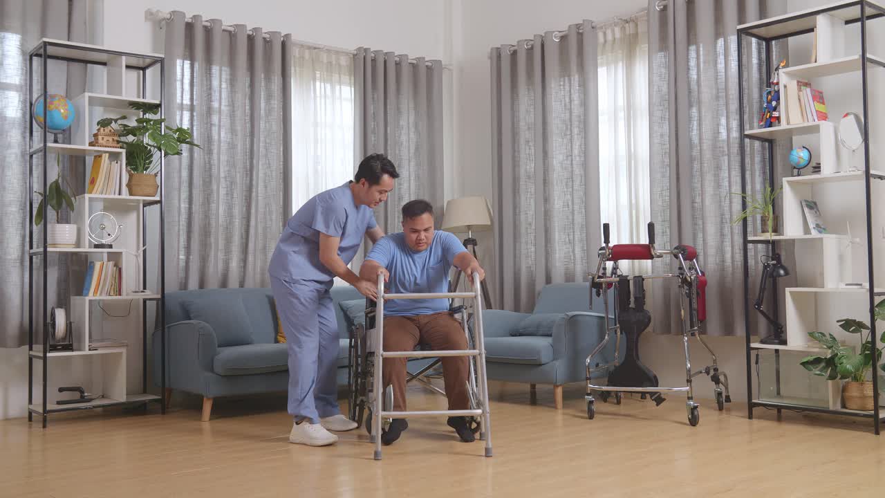 아시안 남성 간호사가 체어에 앉은 환자를 도와 집에서 물리 치료를 하는 동안 러를 사용하여 스스로 서 있습니다.