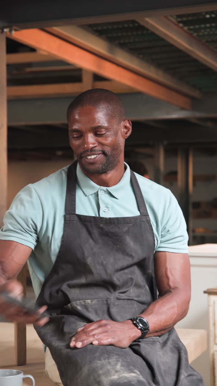 Vertical video: African American man in woodshop on phone call smiling, sipping coffee and walking