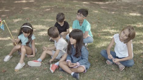 multiethnic children sitting on grass in park together and relaxing