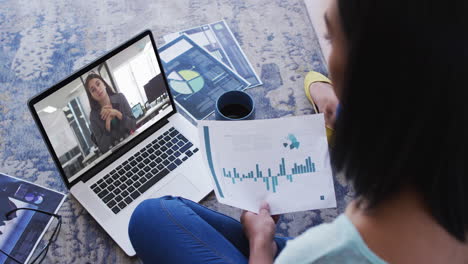 african american woman holding a document having a video call with female colleague on laptop
