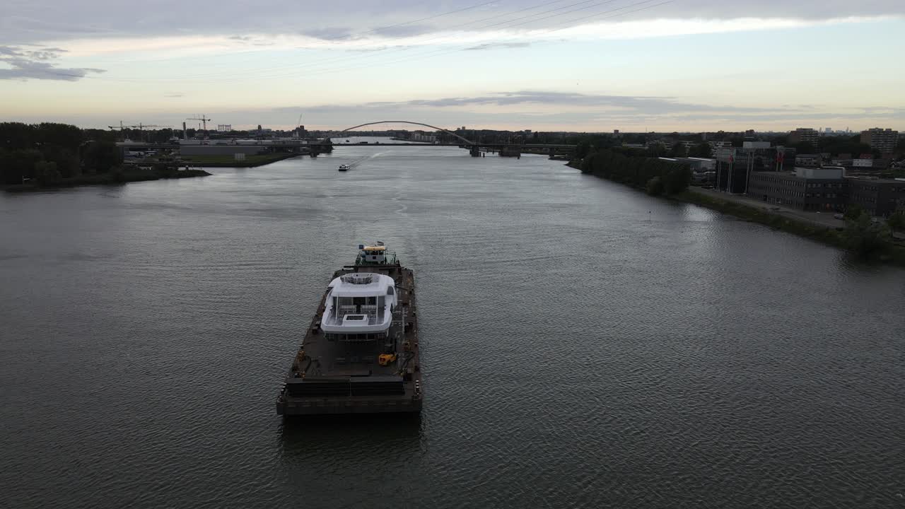 empujador empujando un pontón con el alojamiento blanco de un yate de lujo sobre el río holandés beneden merwede con un puente sobre el agua en el fondo en un día parcialmente nublado