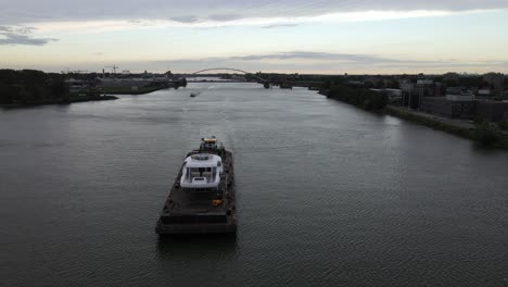 pusher pushing a pontoon with the white accomodation of a luxury yacht over the dutch river beneden merwede with a bridge over the water on the background on a partly cloudy day