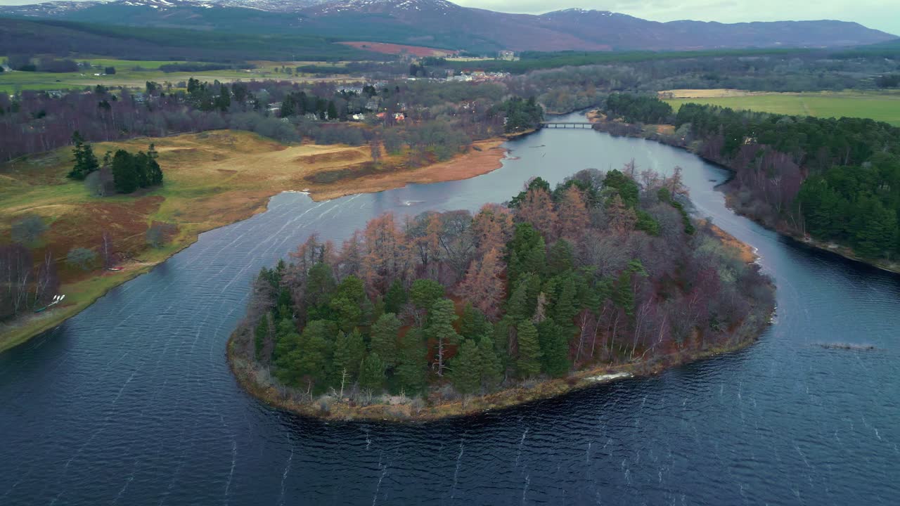 Aerial slide and pan footage of colorful trees on island surrounded by rippled water surface of river