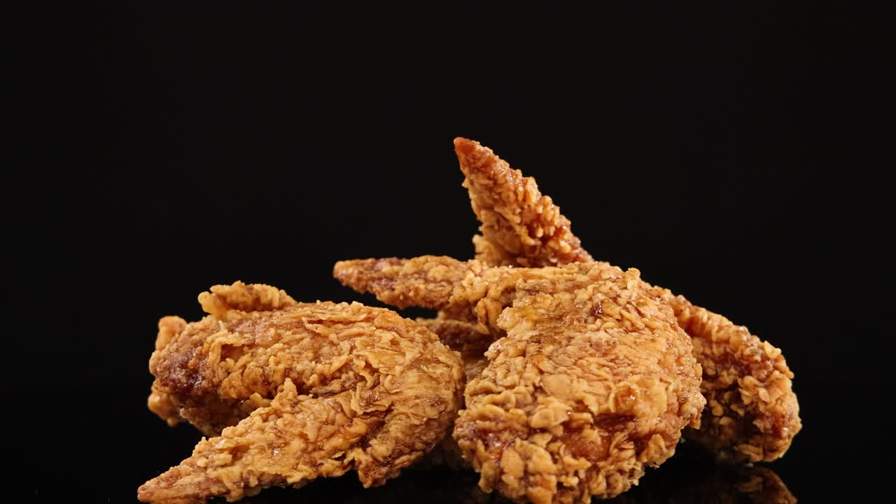 Golden, crispy fried chicken wings rotate smoothly under studio lighting, set against a clean black background for a dramatic, appetizing presentation
