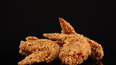 golden, crispy fried chicken wings rotate smoothly under studio lighting, set against a clean black background for a dramatic, appetizing presentation