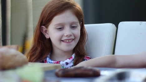 Young-smiling-girl-thanking-Dad-for-her-food-at-backyard-picnic-with-her-family