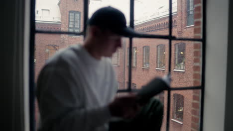 Lectura-Individual-Enfocada-Junto-A-Una-Ventana-Helada,-Con-Un-Histórico-Edificio-De-Ladrillo-Como-Telón-De-Fondo-En-Un-Día-Invernal