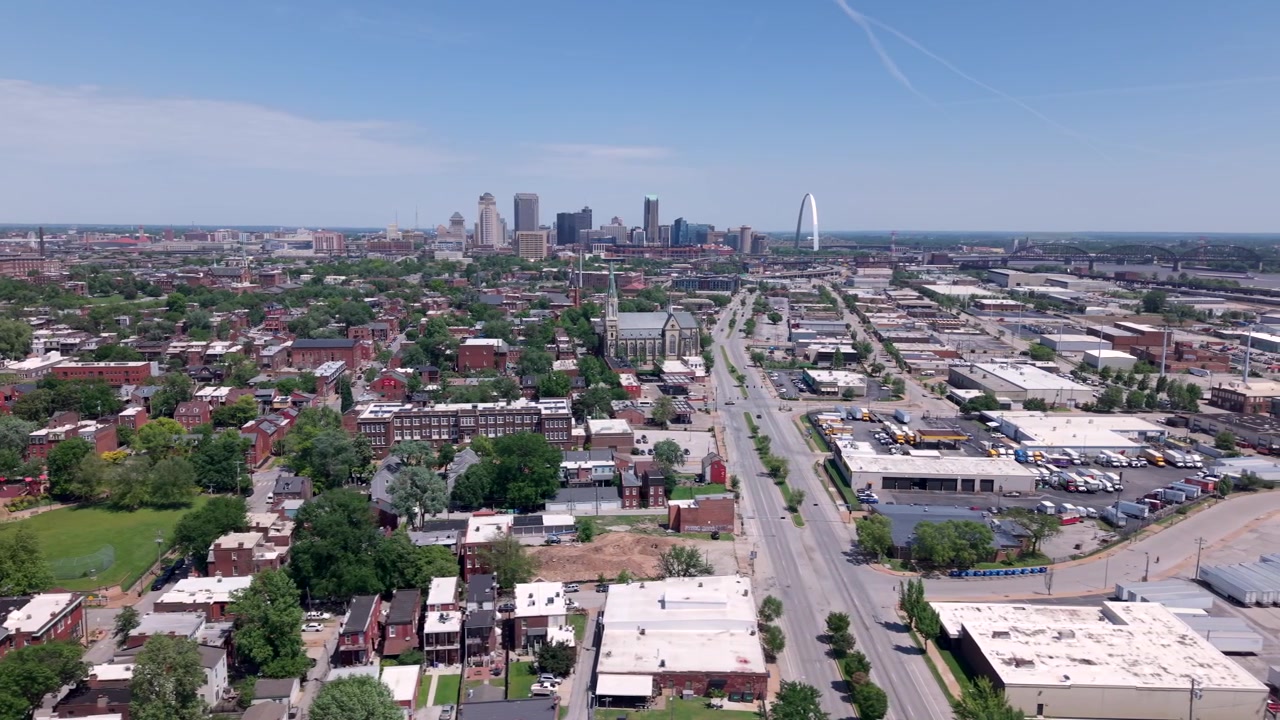 Skyline della città di St. Louis, Missouri, con l'iconico Gateway Arch, quartieri urbani, spazi verdi e cieli blu vivido in una luminosa giornata estiva, sorvolo aereo.