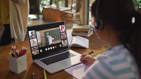 schoolgirl using laptop for online lesson at home, with diverse teacher and class on screen