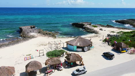 cars parked at beachside souvenir shops on cozumel island in mexico overlooking tropical turquoise beach, aerial