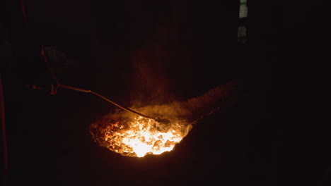 illuminated molten metal being stirred in a dark foundry environment