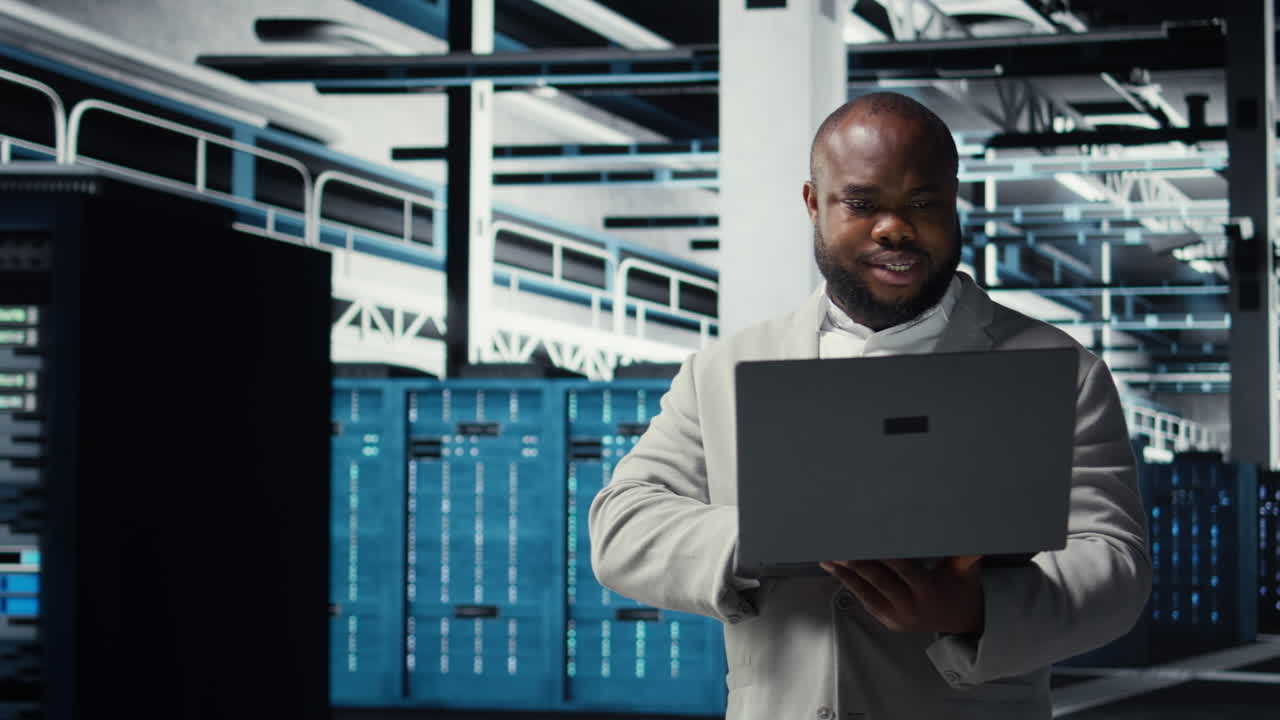 Vertical video Smiling engineer in data center managing software using laptop