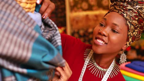 mujer tanzaniana con un turbante con estampado de serpiente sobre el oído trabajando en una tienda de telas
