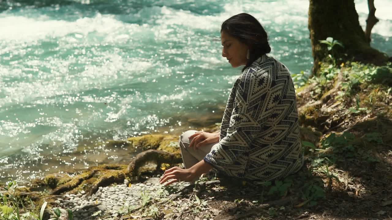 mujer meditando junto a un río en un bosque