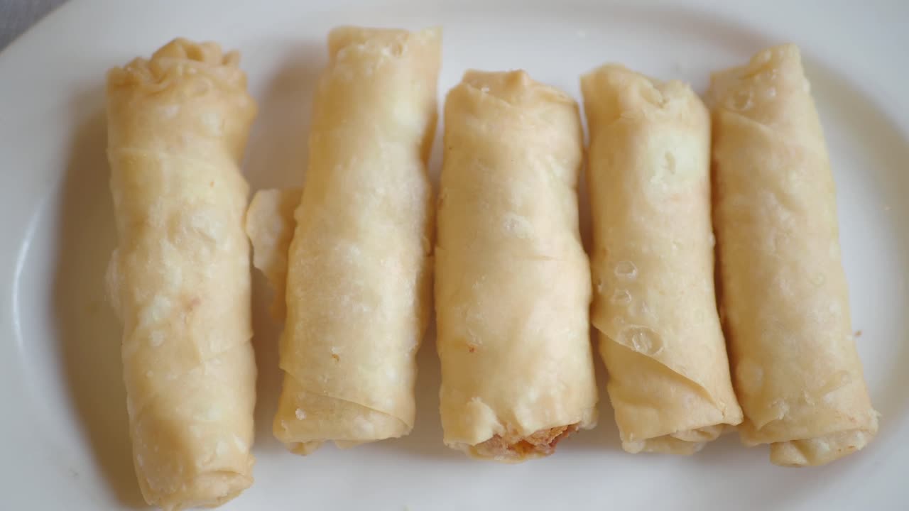 Hand picking up a fried spring roll from a plate of snacks