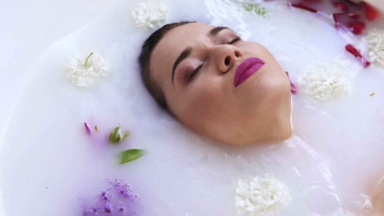 Close Up view of young woman's face bathing in milk bath filled with flowers and getting up. Spa and skin care concept