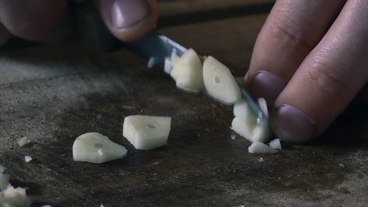 Close up of a mans fingers cutting garlic into pieces with a knife