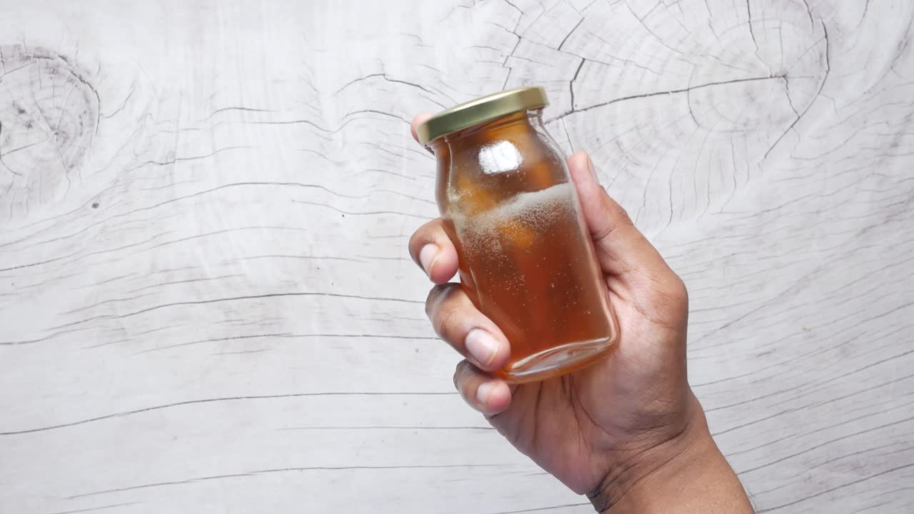 mano sosteniendo un pequeño frasco de vidrio de miel