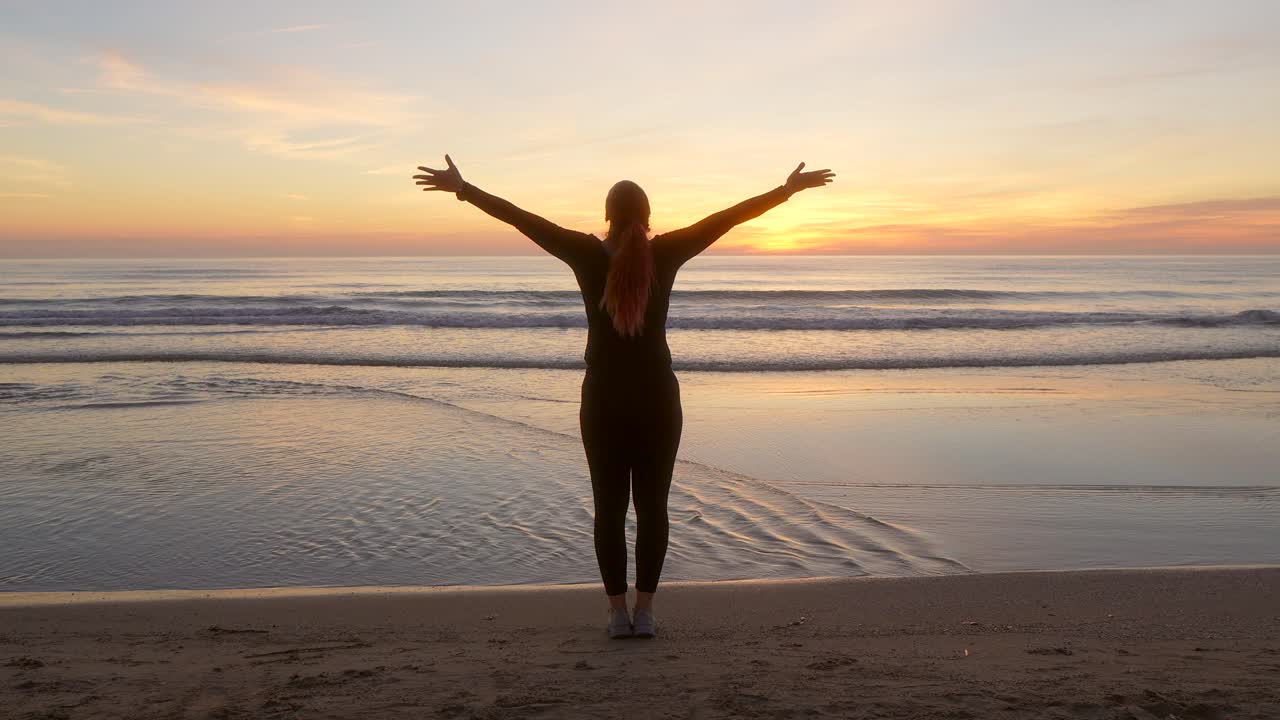 mujer abriendo los brazos y viendo el amanecer mientras respira mientras contempla el mar