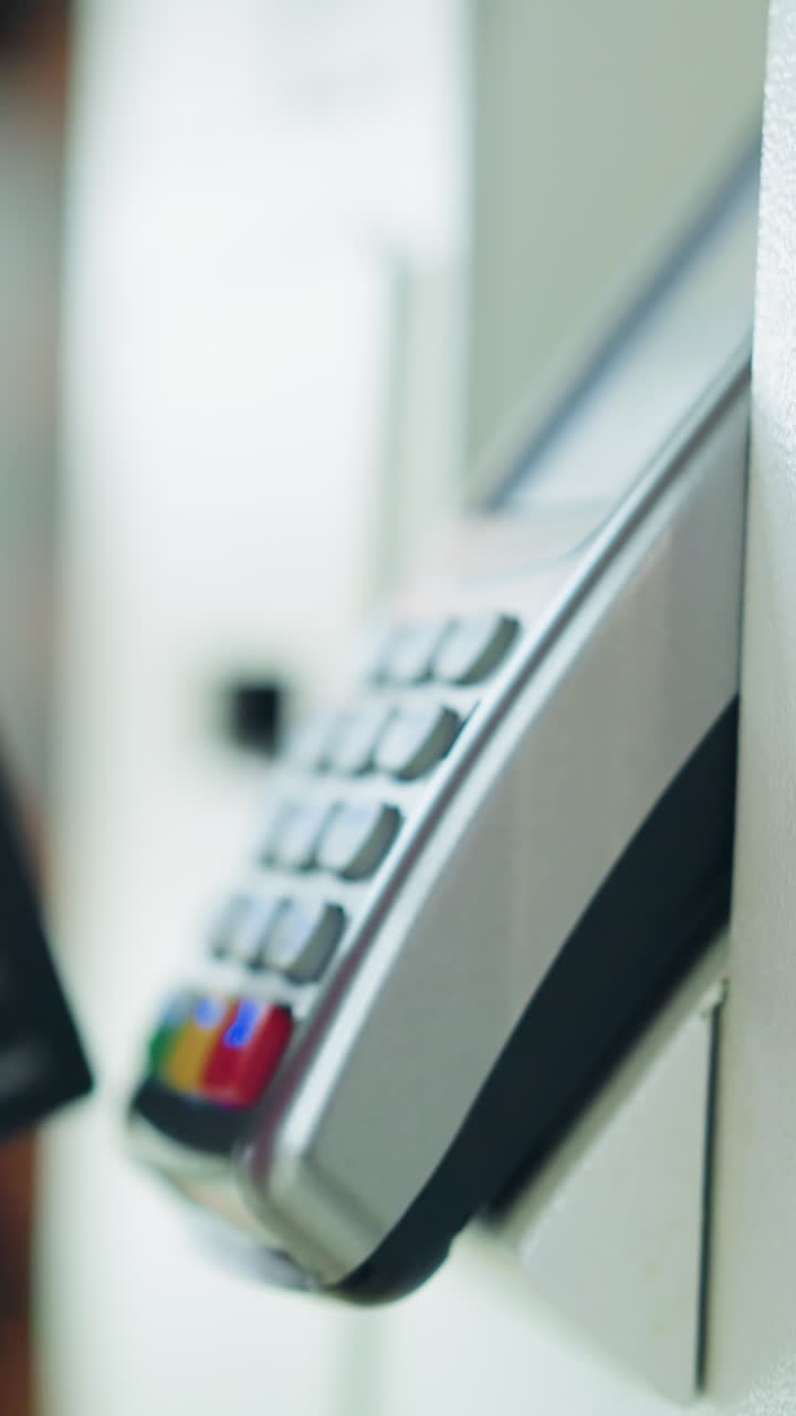 dama de camisa rosa con una cadena de muñeca desliza una tarjeta negra en un cajero automático blanco para completar una transacción de pago, con artículos poco claros en el fondo, el fondo está borroso